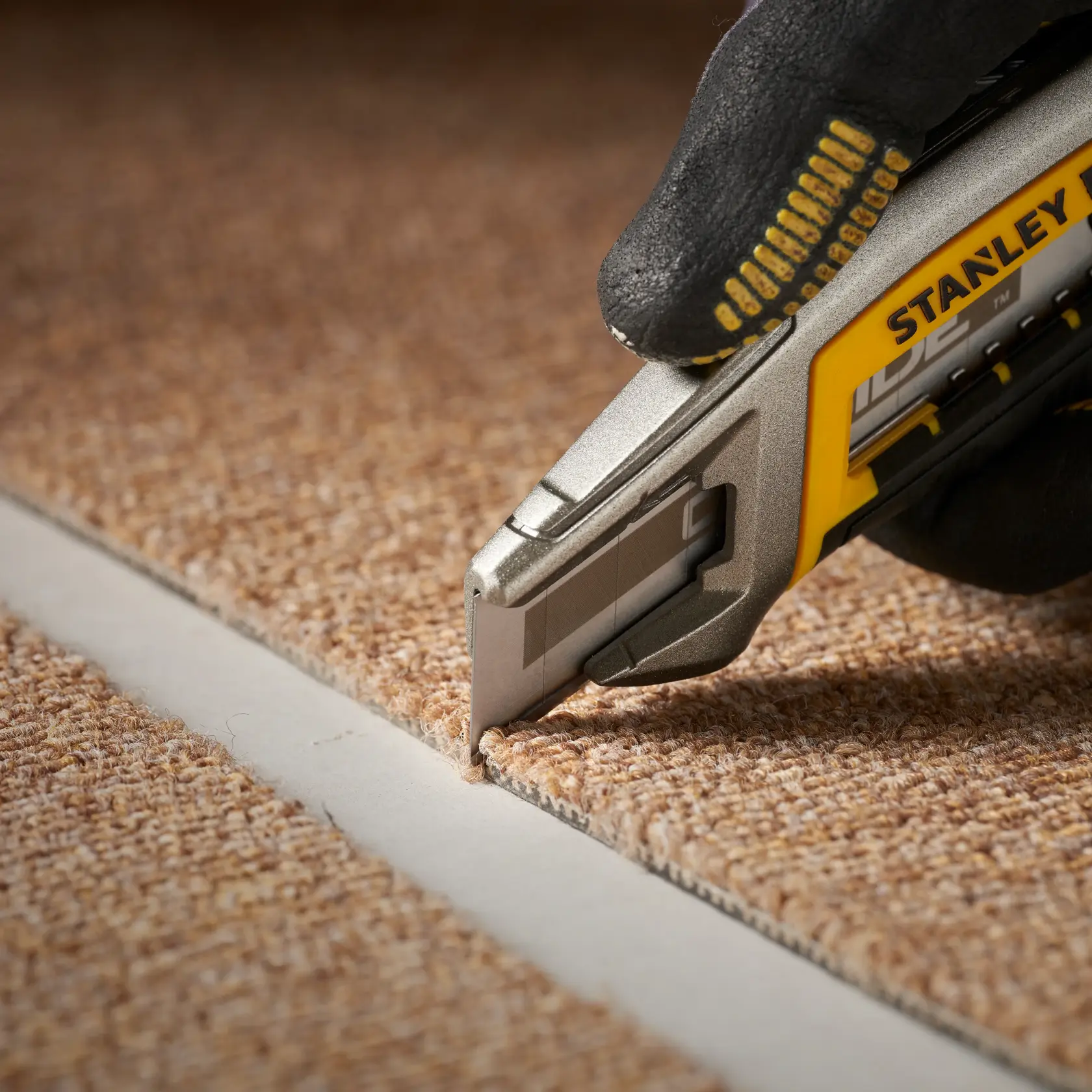 STANLEY STHT0-11818 utility knife cutting brown carpet, close-up photography.