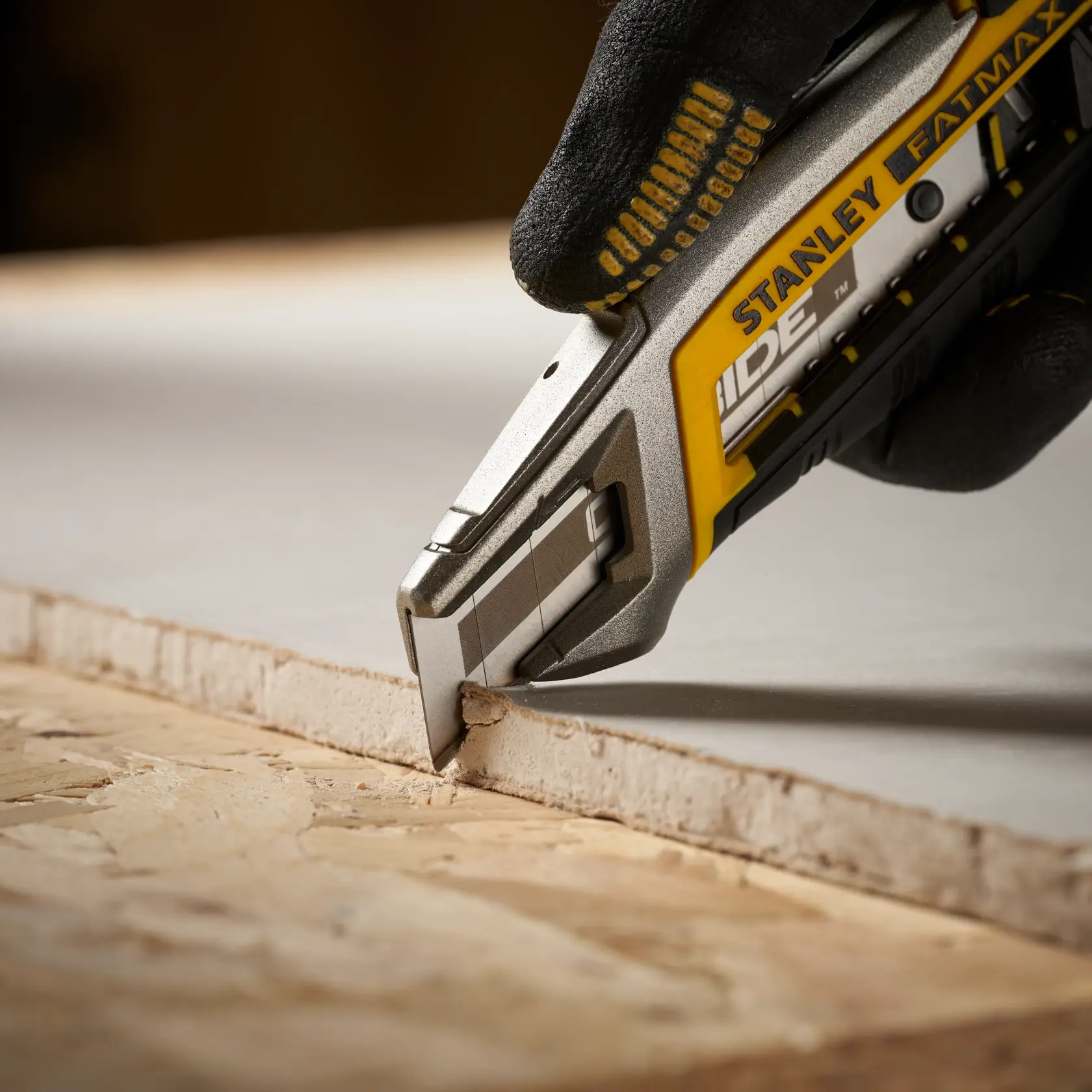 Photo of STANLEY STHT0-11818 utility knife cutting drywall, close-up detail, yellow and silver handle.