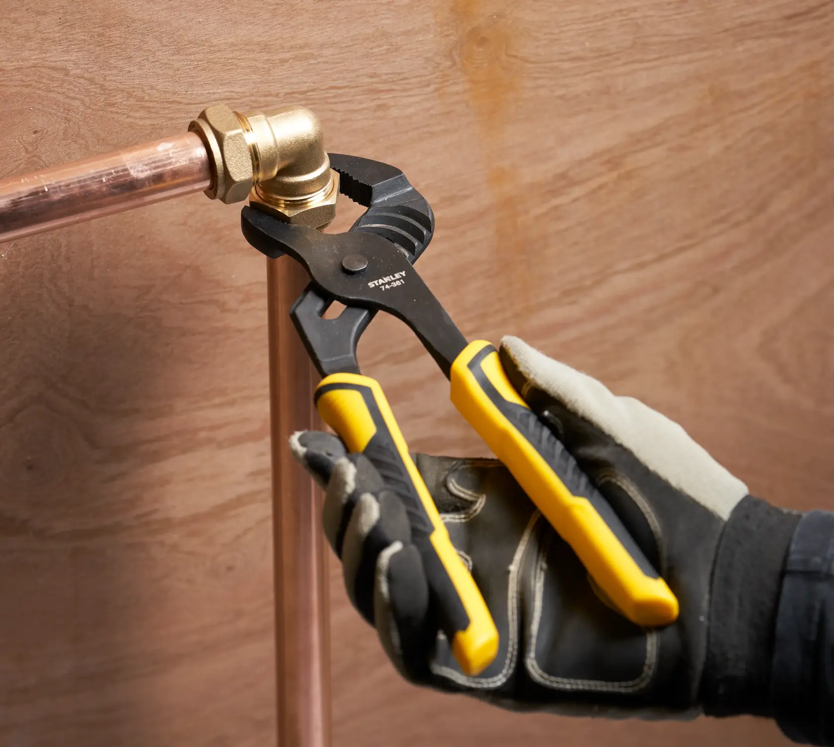 Photo of STANLEY STHT0-74361 slip joint pliers with yellow handles, adjusting copper pipe fitting.