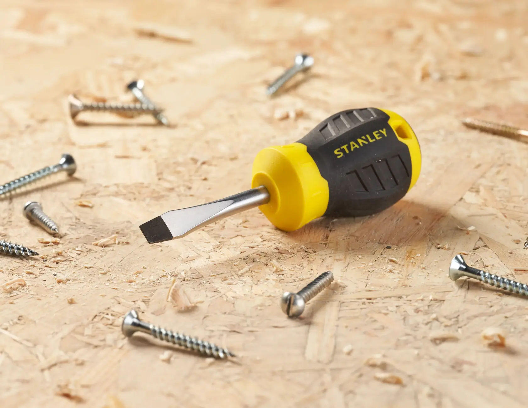 STANLEY STHT16147-0 stubby flathead screwdriver with yellow and black handle on wood with screws, angled view.