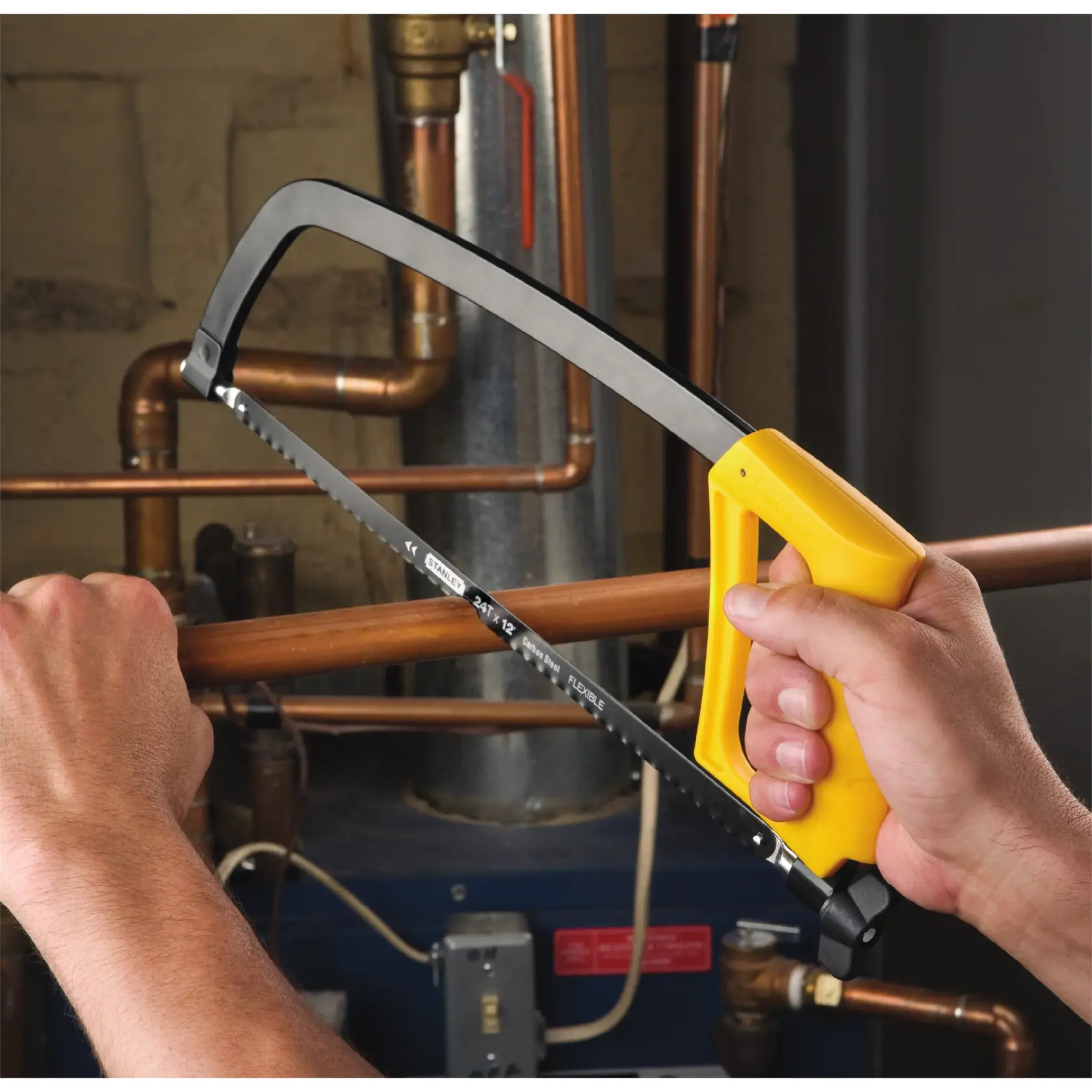 STANLEY STHT20138 hacksaw with yellow handle cutting copper pipe in plumbing context.