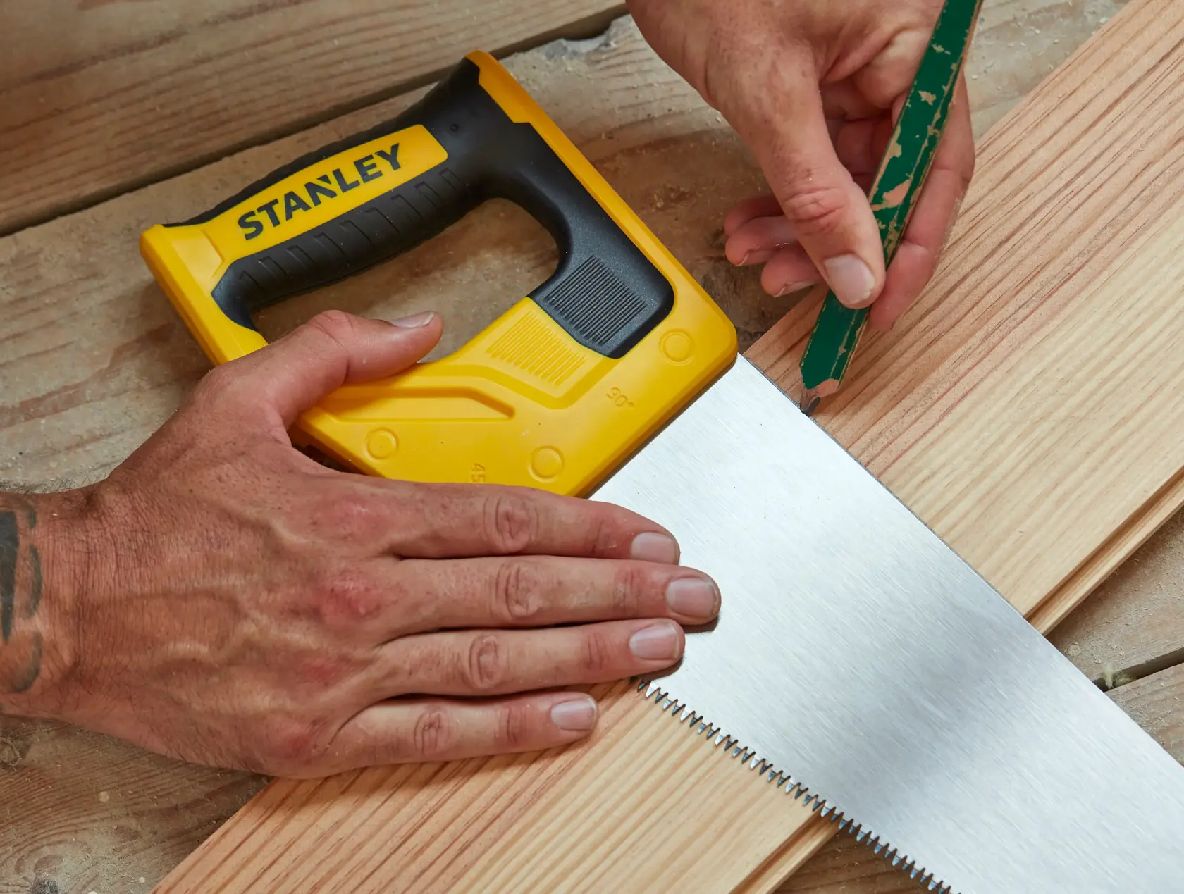 STANLEY STHT20351-1 hand saw with yellow and black handle on wood, close-up during marking process.