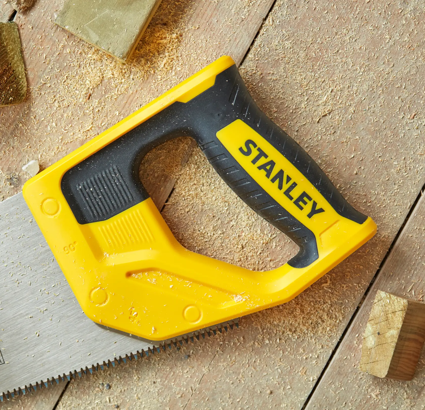 STANLEY STHT20351-1 hand saw with yellow and black handle, close-up on wood and sawdust.