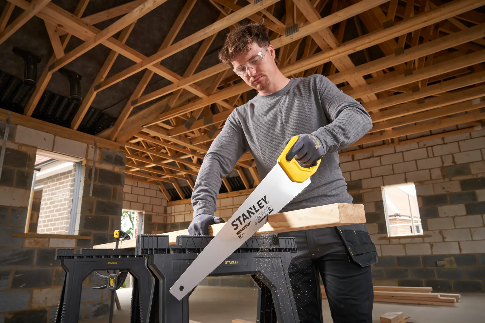 Photo of STANLEY STHT20368-1 hand saw with yellow handle cutting wood on black sawhorse in construction site.