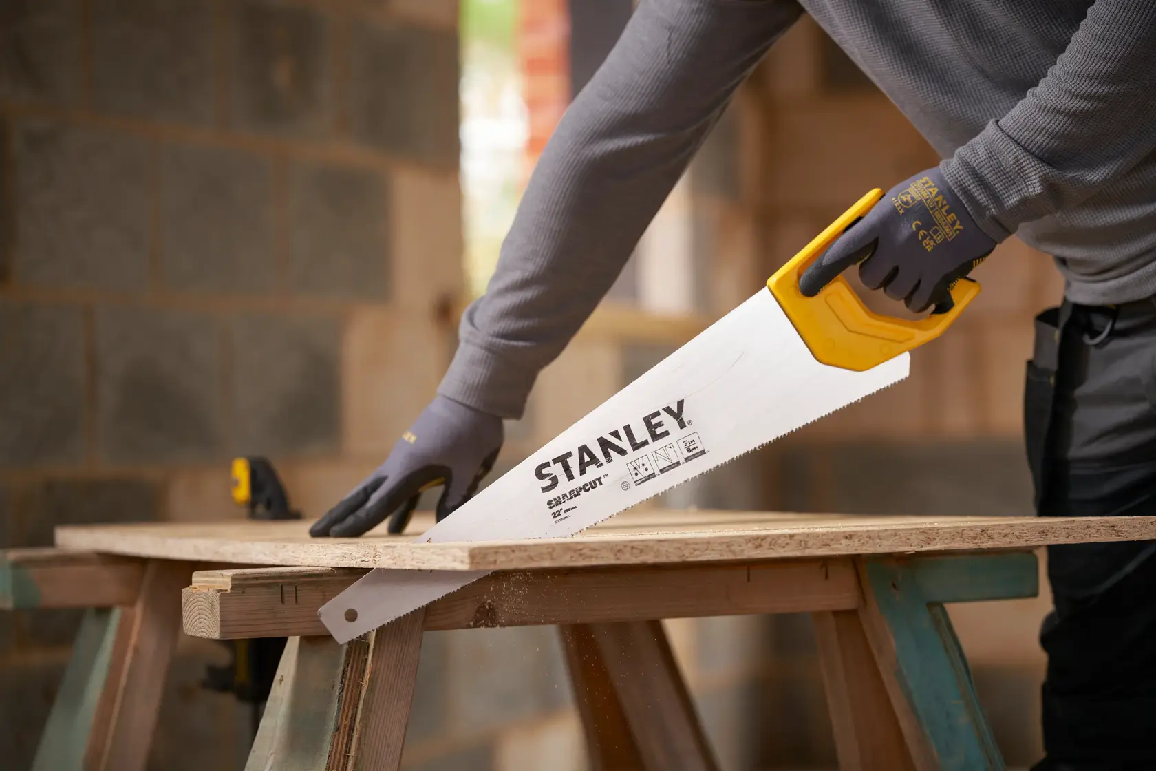 Photo of STANLEY STHT20368-1 hand saw with yellow handle cutting wood in a construction setting.