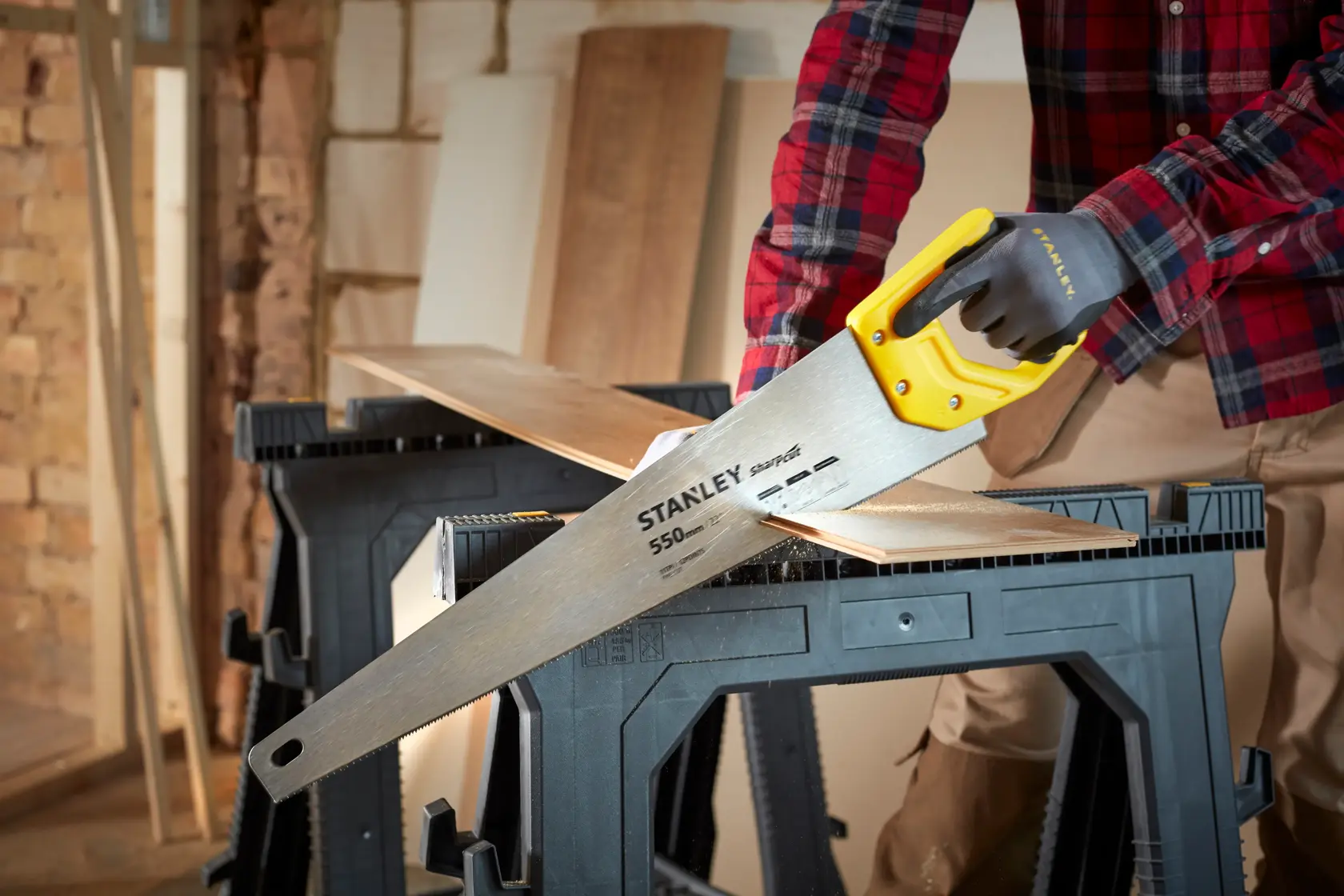 STANLEY STHT20372-1 hand saw with yellow handle cutting wood in workshop setting.