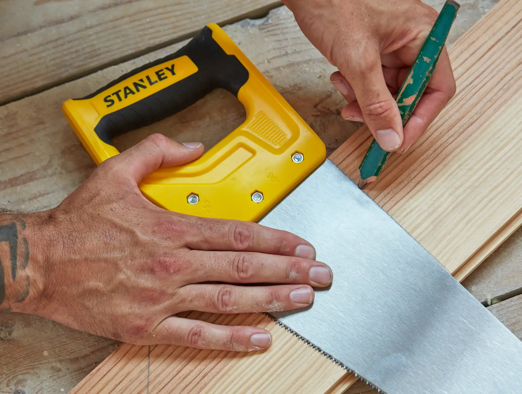 STANLEY STHT20372-1 hand saw with yellow handle on wood, pencil marking cut line, close-up photography.