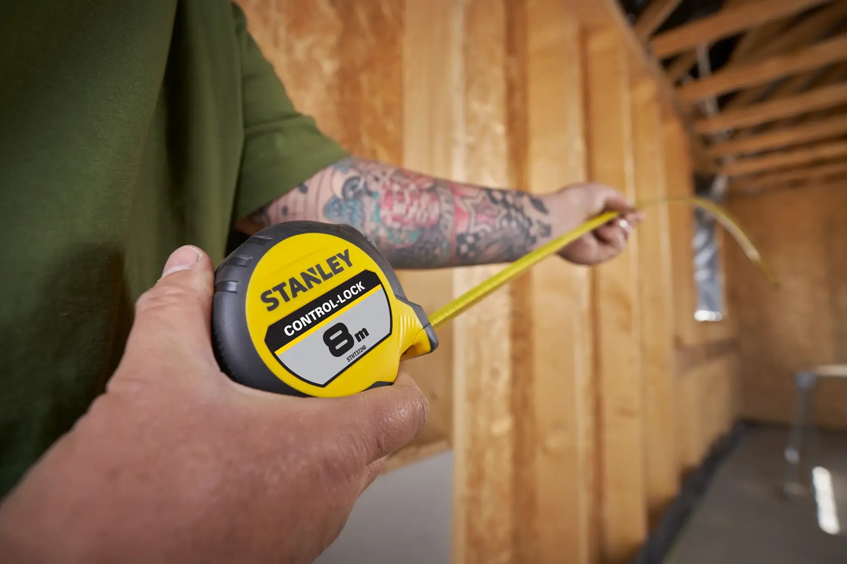 Photo of a STANLEY STHT37240 tape measure being extended by a person in a wooden construction site.