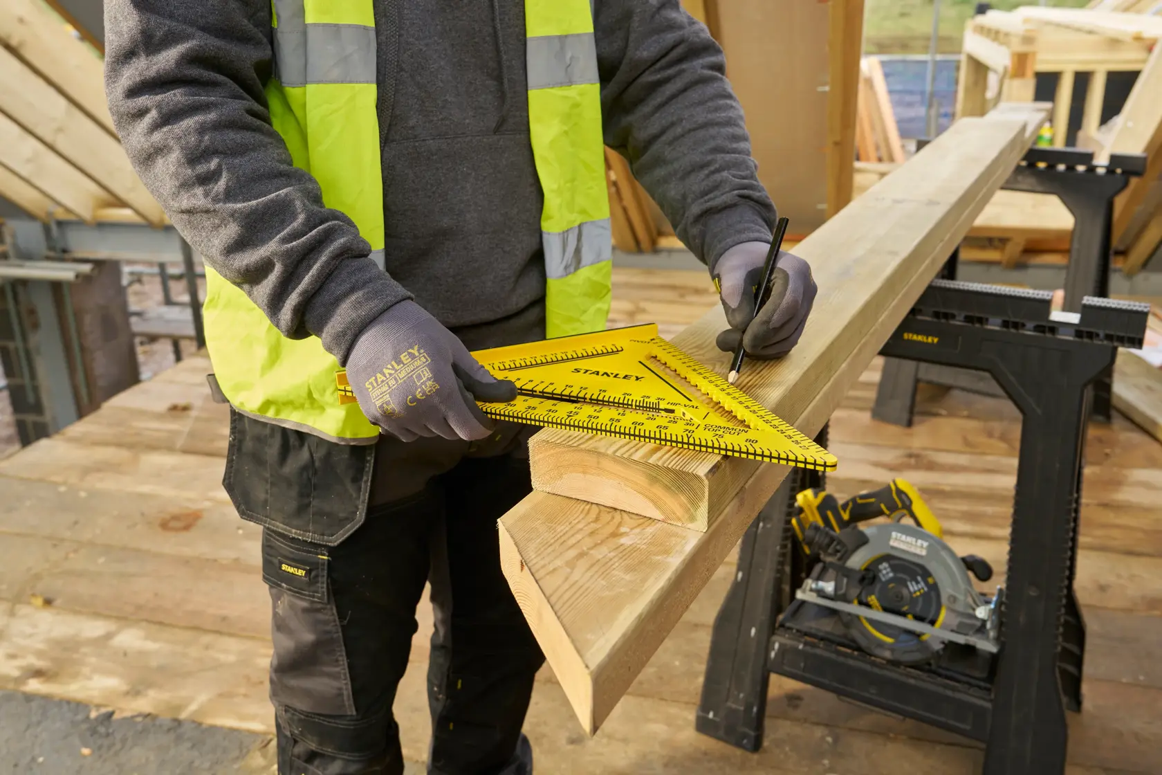 STANLEY STHT46013-0 yellow rafter square used for marking wood on construction site, worker wearing gloves.