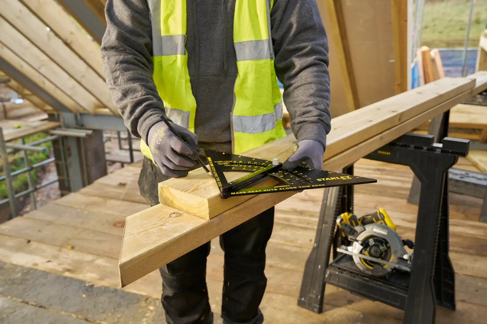 STANLEY STHT46054-0 carpenter using black and yellow framing square to mark wood, construction site background.