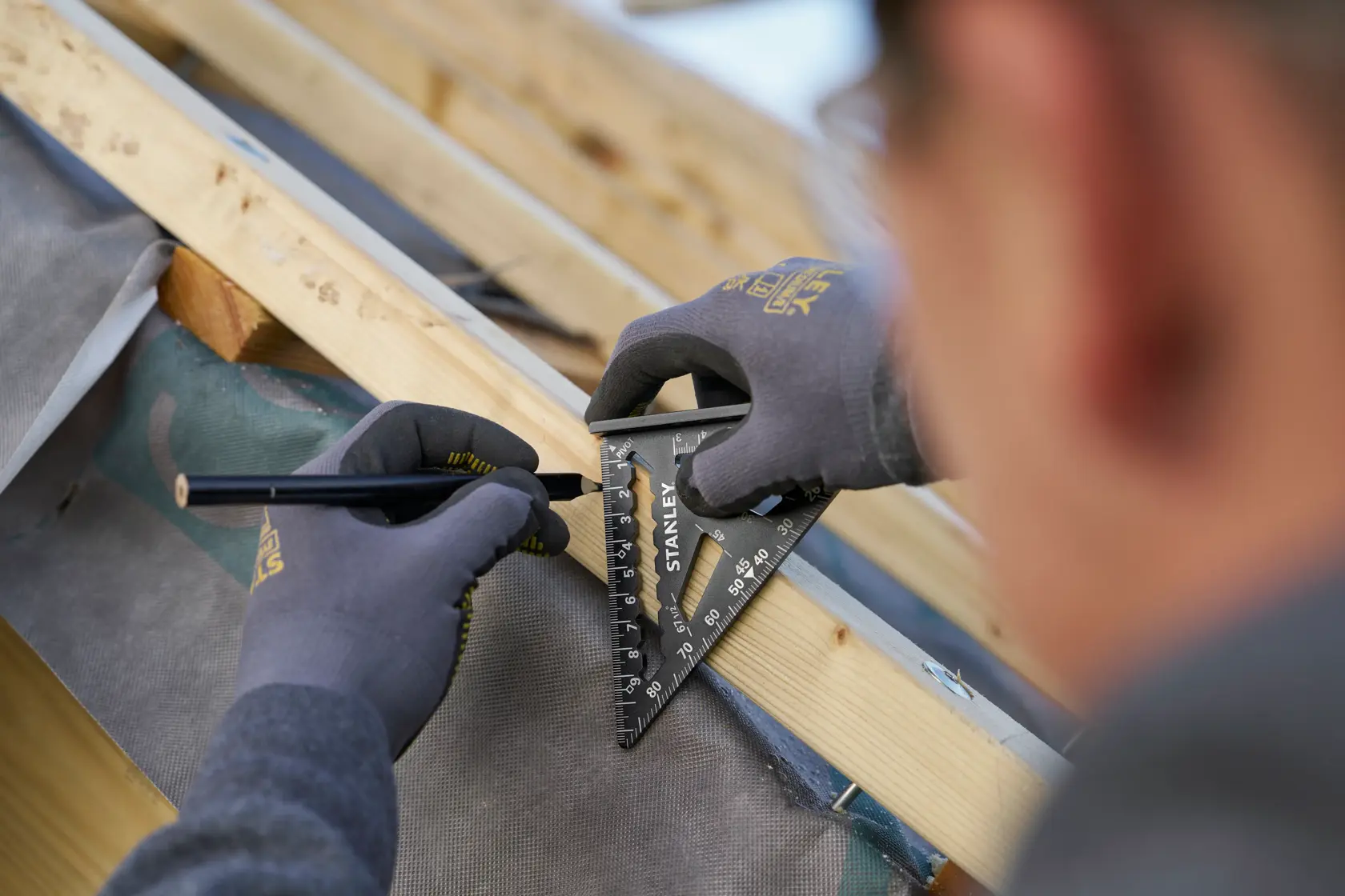 Photo of STANLEY STHT46100-0 rafter square in use marking wood, close-up on hands wearing gloves.