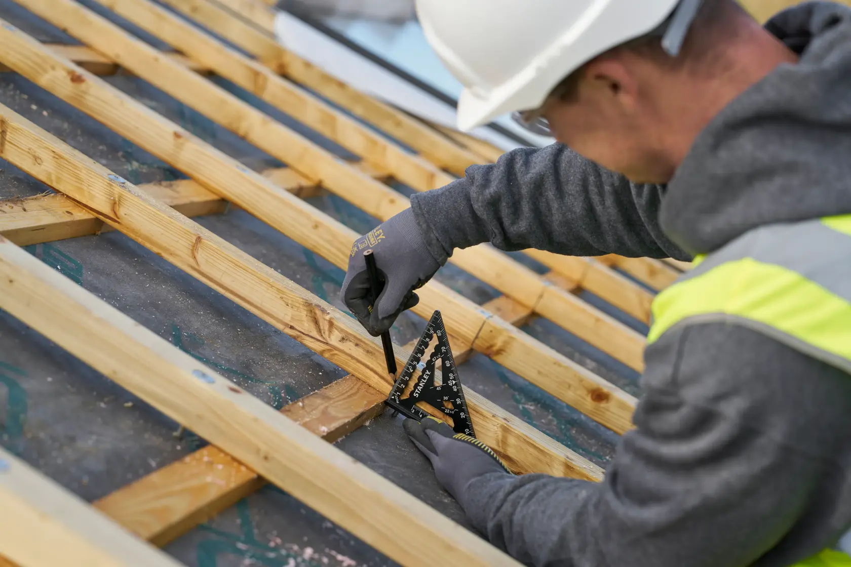 Photo of STANLEY STHT46100-0 black carpenter's square in use on wooden beams, close-up construction scene.