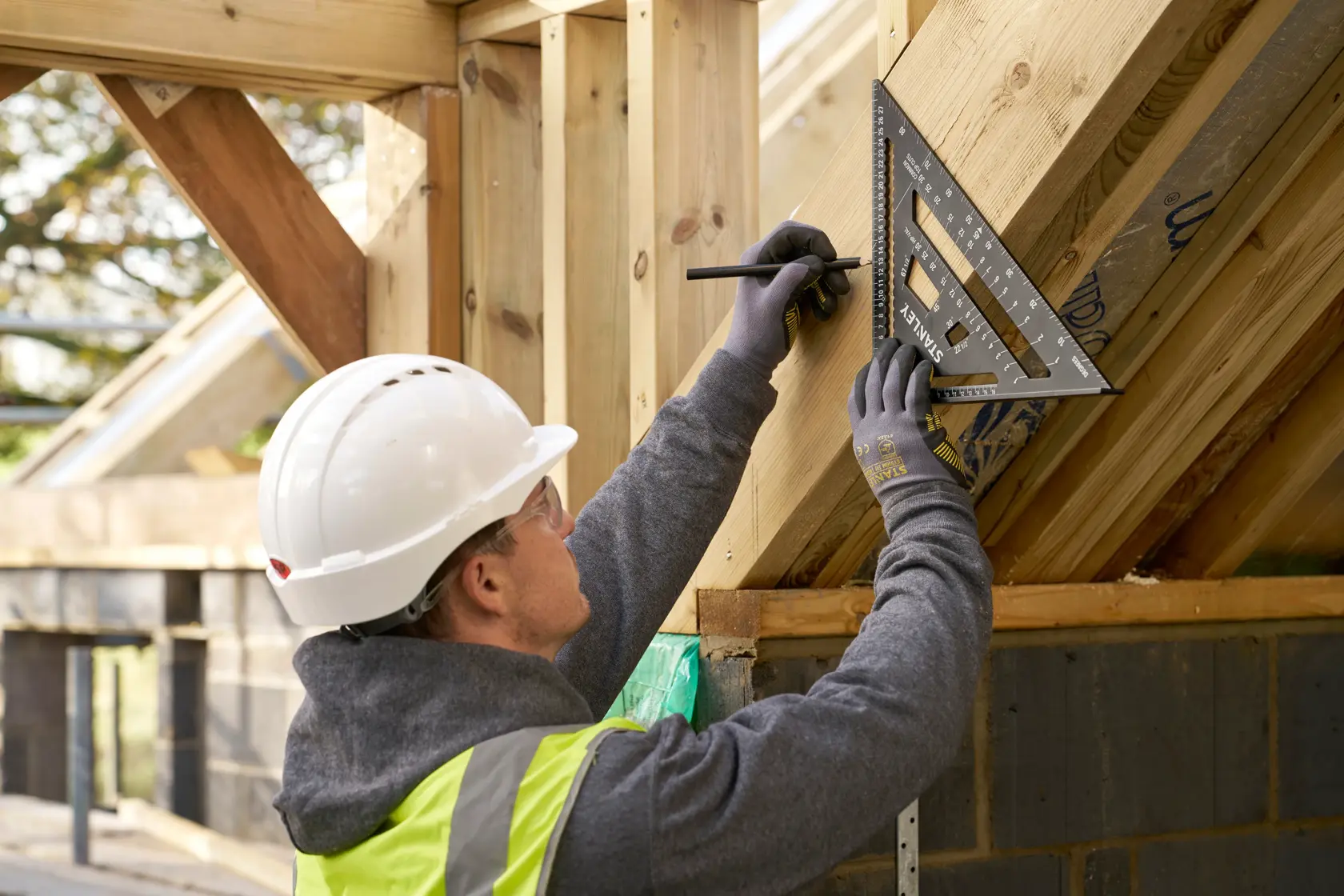 STANLEY STHT46102-0 rafter square used by worker marking wood frame on construction site.
