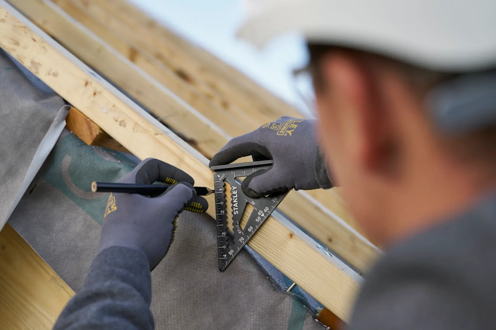 Photo of a person using a STANLEY STHT46103-0 rafter square to mark measurements on a wooden beam during construction.
