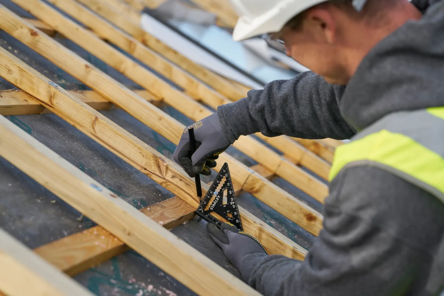 STANLEY STHT46103-0 rafter square in use on wooden roof frame, person marking wood with pencil, outdoor worksite.