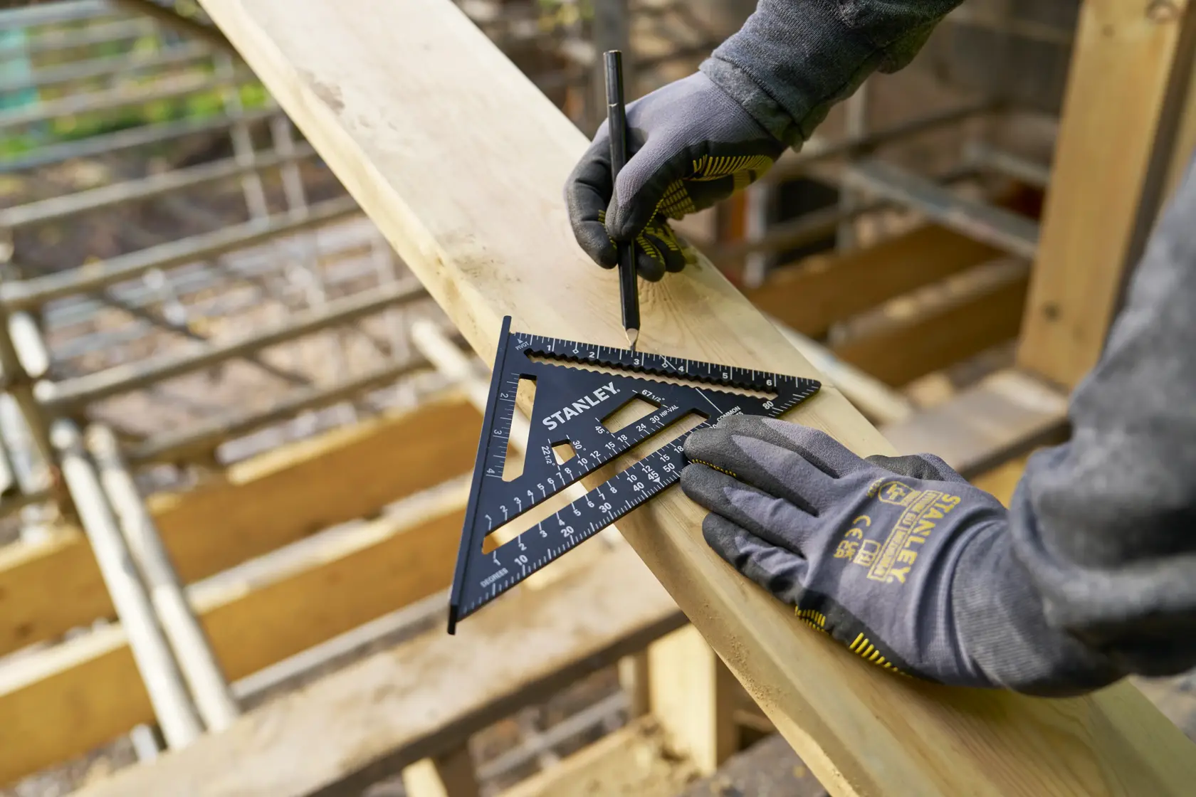 STANLEY STHT46104-0 rafter square used for marking on wood by a gloved hand, construction site background.
