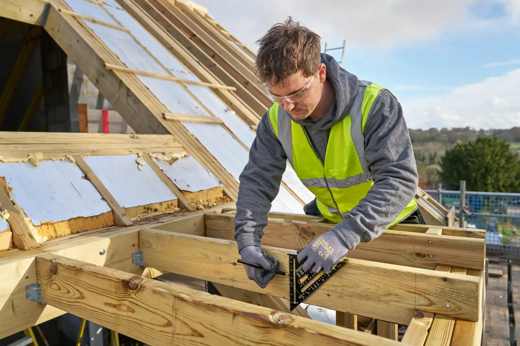 STANLEY STHT46104-0 roofing square tool in use on wooden beams at a construction site.