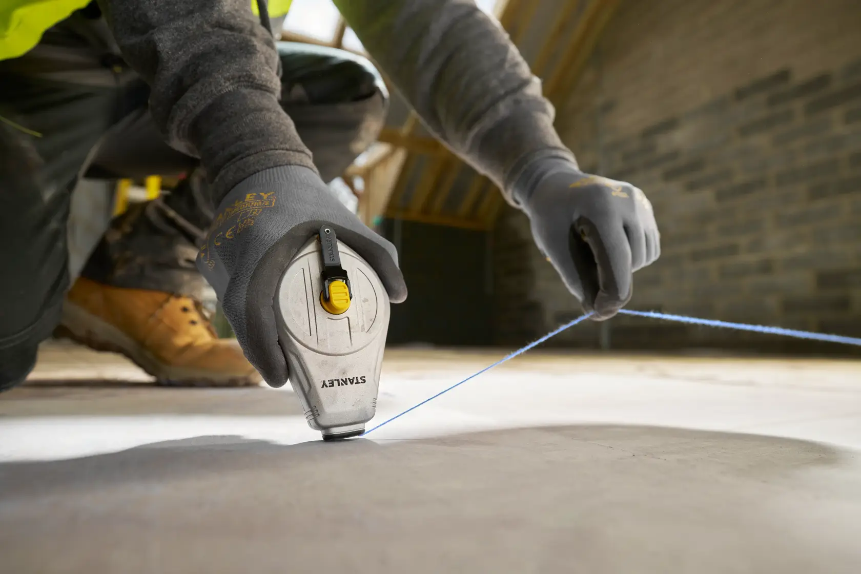 STANLEY STHT47110-0 chalk line being used on a construction site, close-up of hands with gloves pulling blue line.