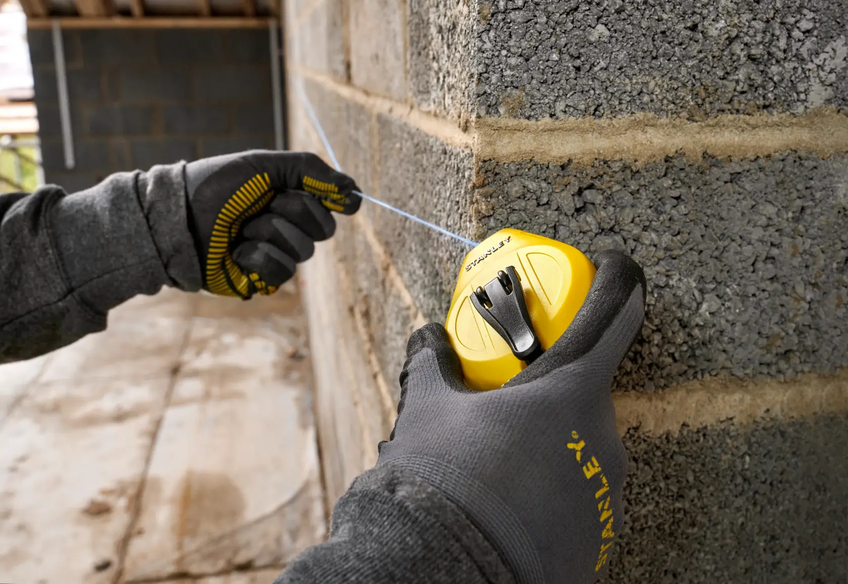 STANLEY STHT47112-0 chalk line reel used on a concrete wall, worker wearing gloves, close-up photography.