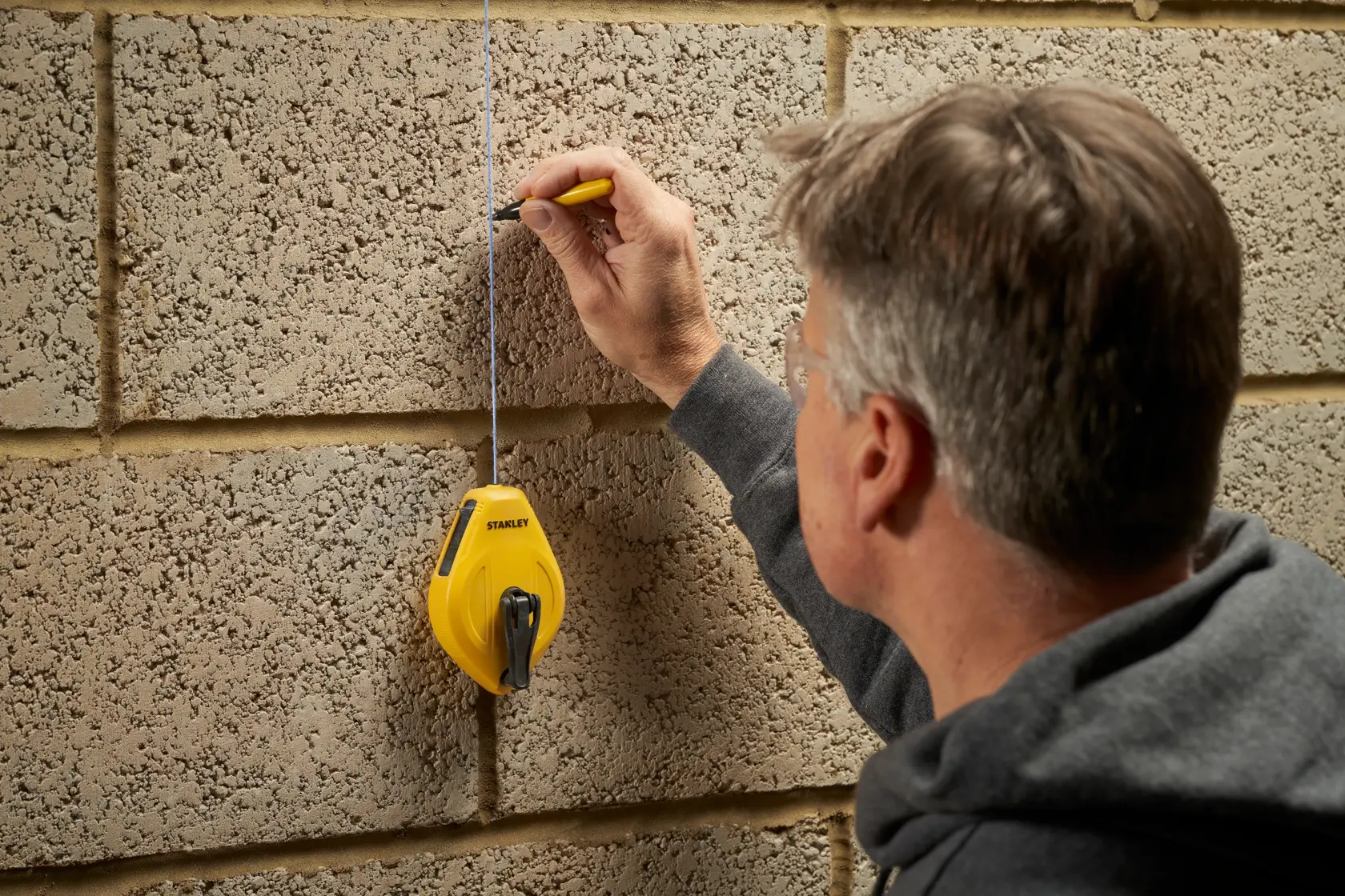 Photo of STANLEY STHT47112-0 chalk line reel marking a straight line on a concrete wall, side view.