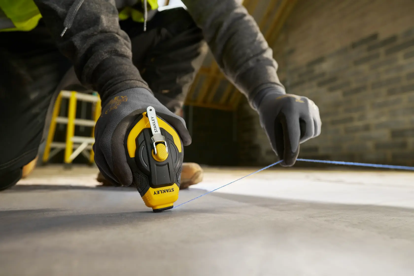 Photo of STANLEY STHT47311-0 chalk line tool in use, worker marking line on concrete floor.