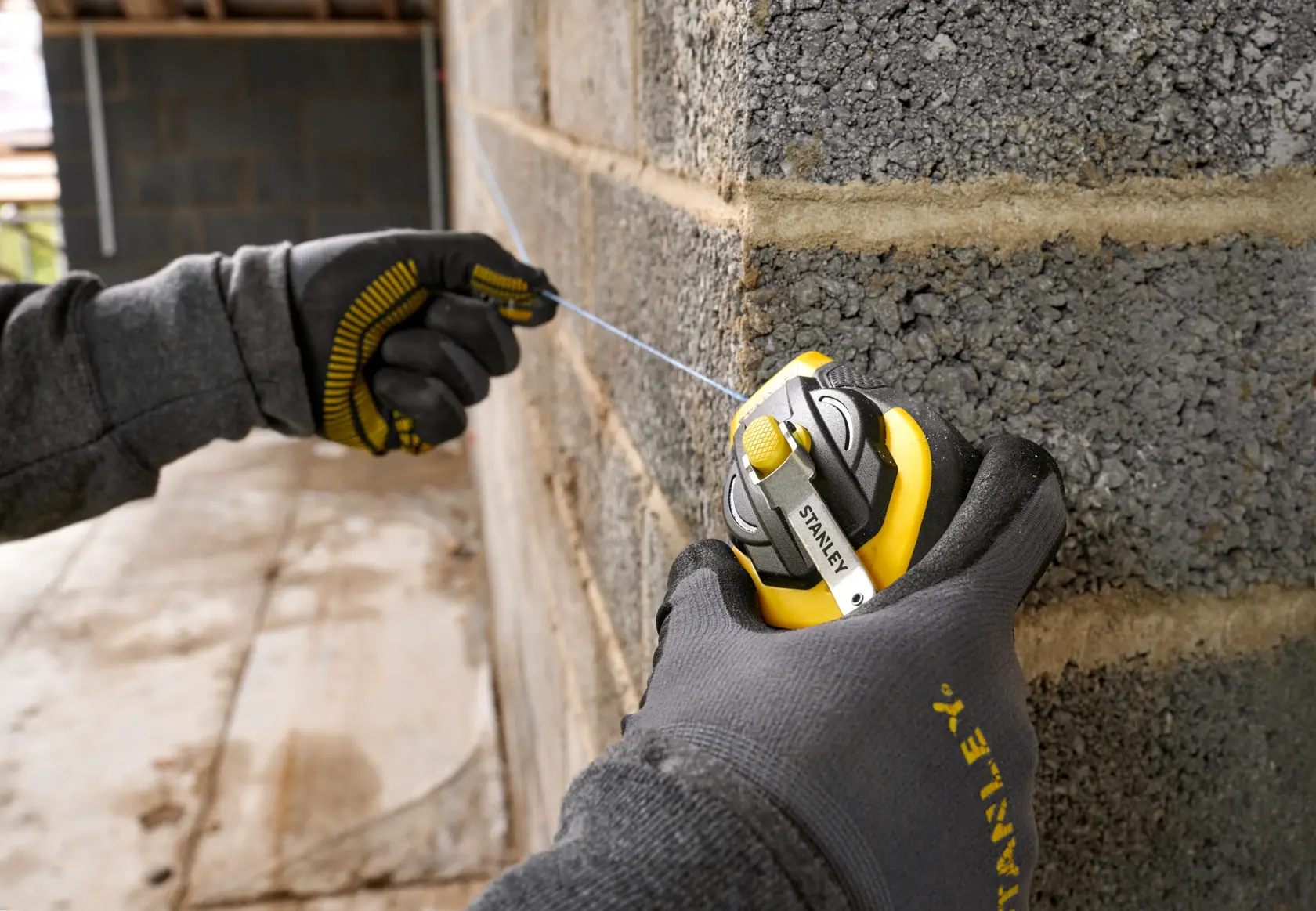 STANLEY STHT47311-0 chalk line reel in use on a brick wall, close-up of gloved hands pulling the blue line.