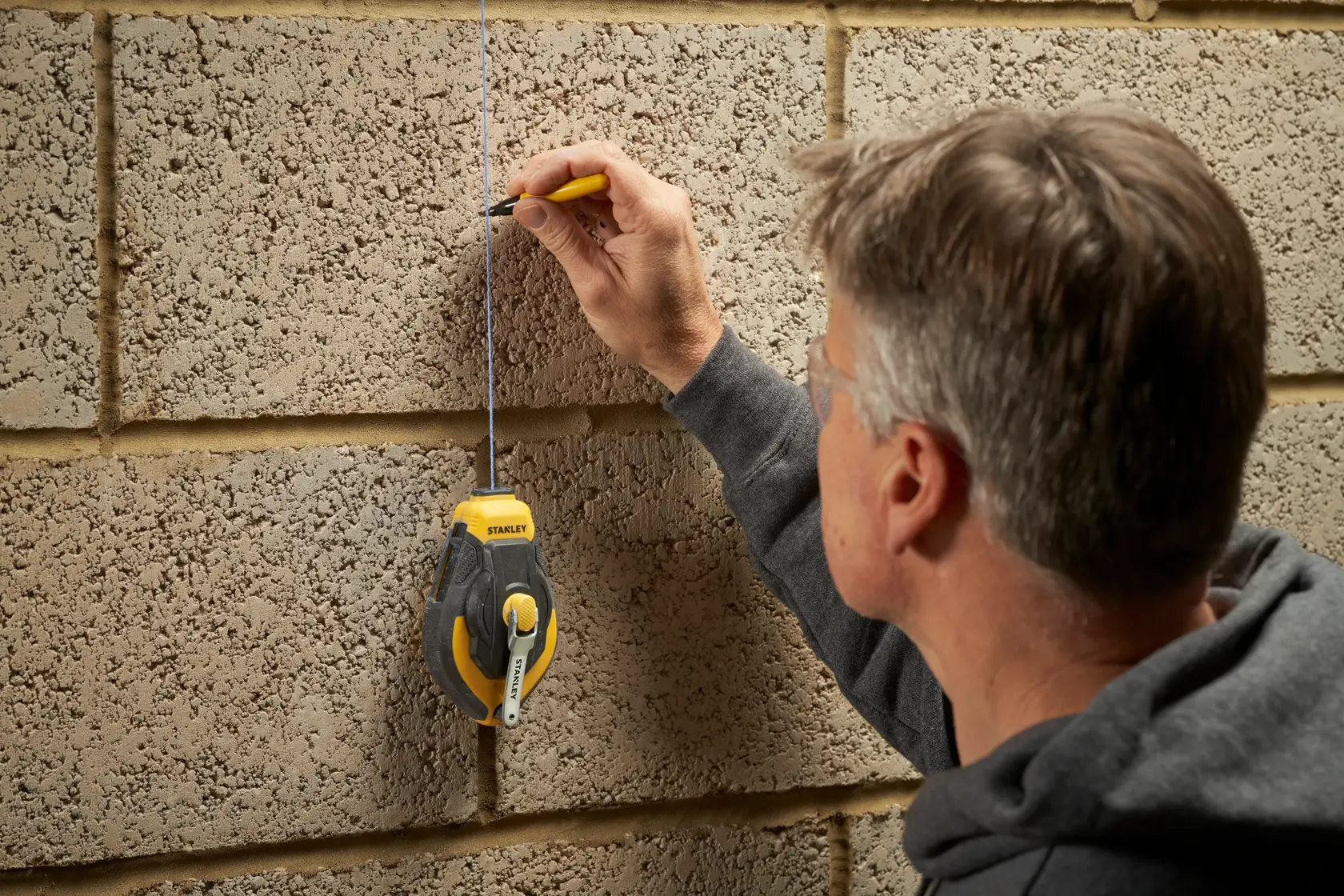 Photo of person marking a brick wall with a pencil using a STANLEY STHT47311-0 chalk line, product category photography.