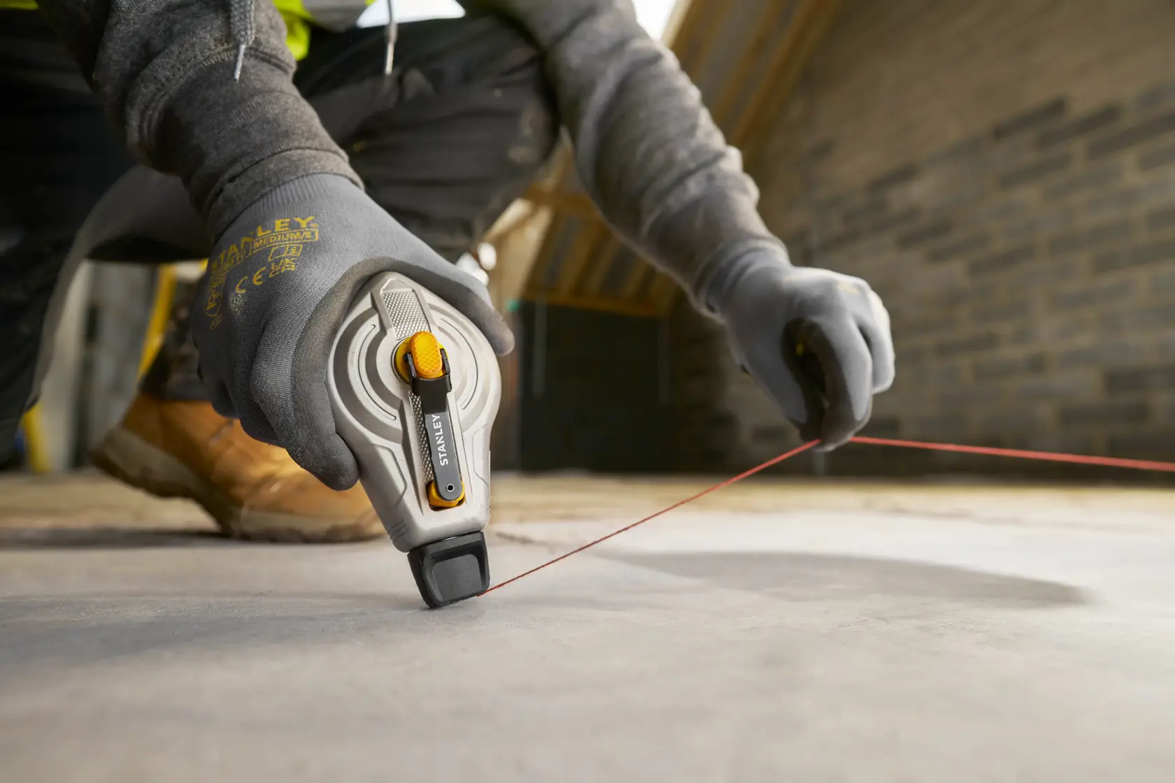 Photo of STANLEY STHT47611-0 chalk line reel in use on construction site floor, worker wearing gloves.