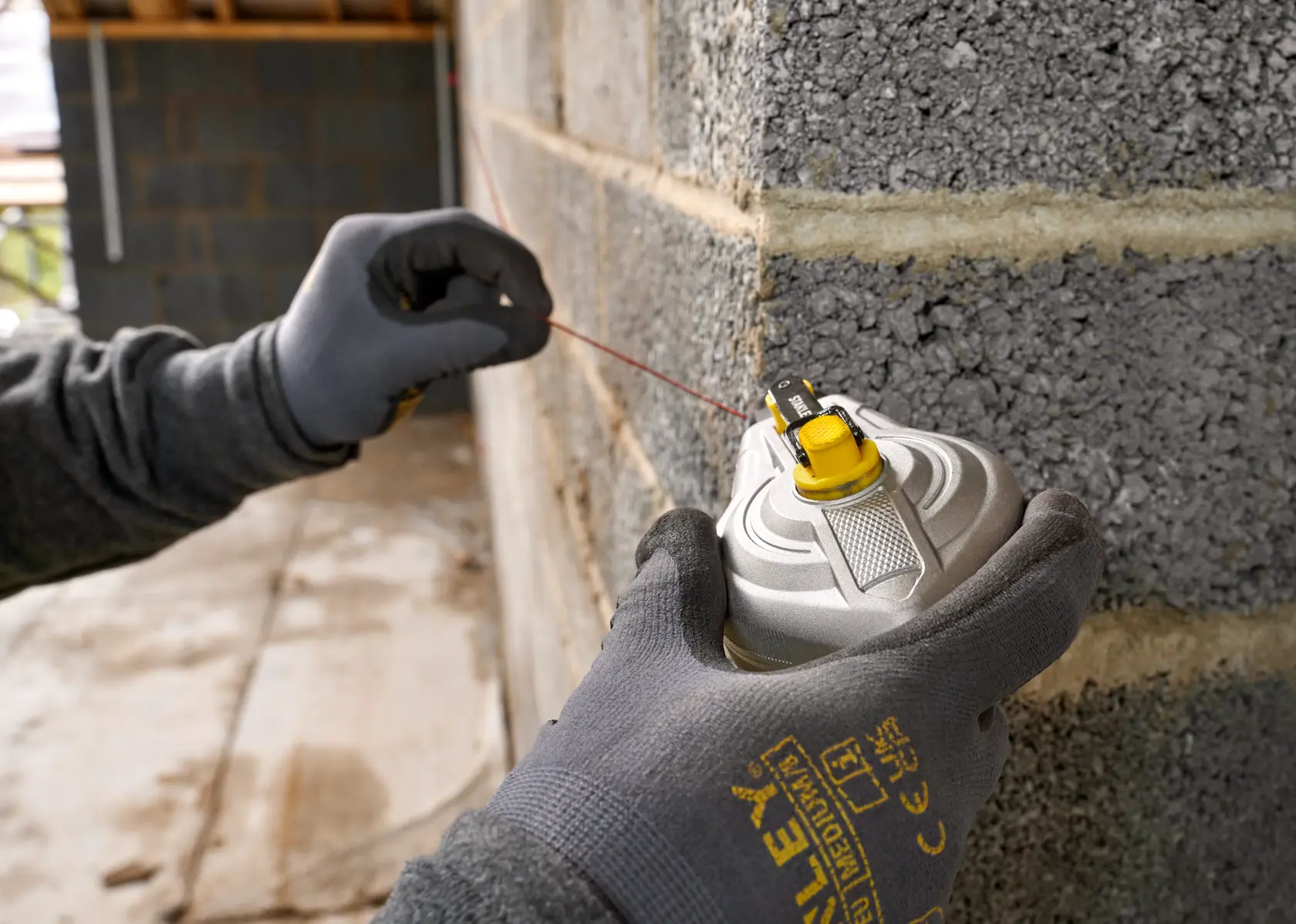 STANLEY STHT47611-0 chalk line tool held by gloved hand against a masonry wall, close-up photography.