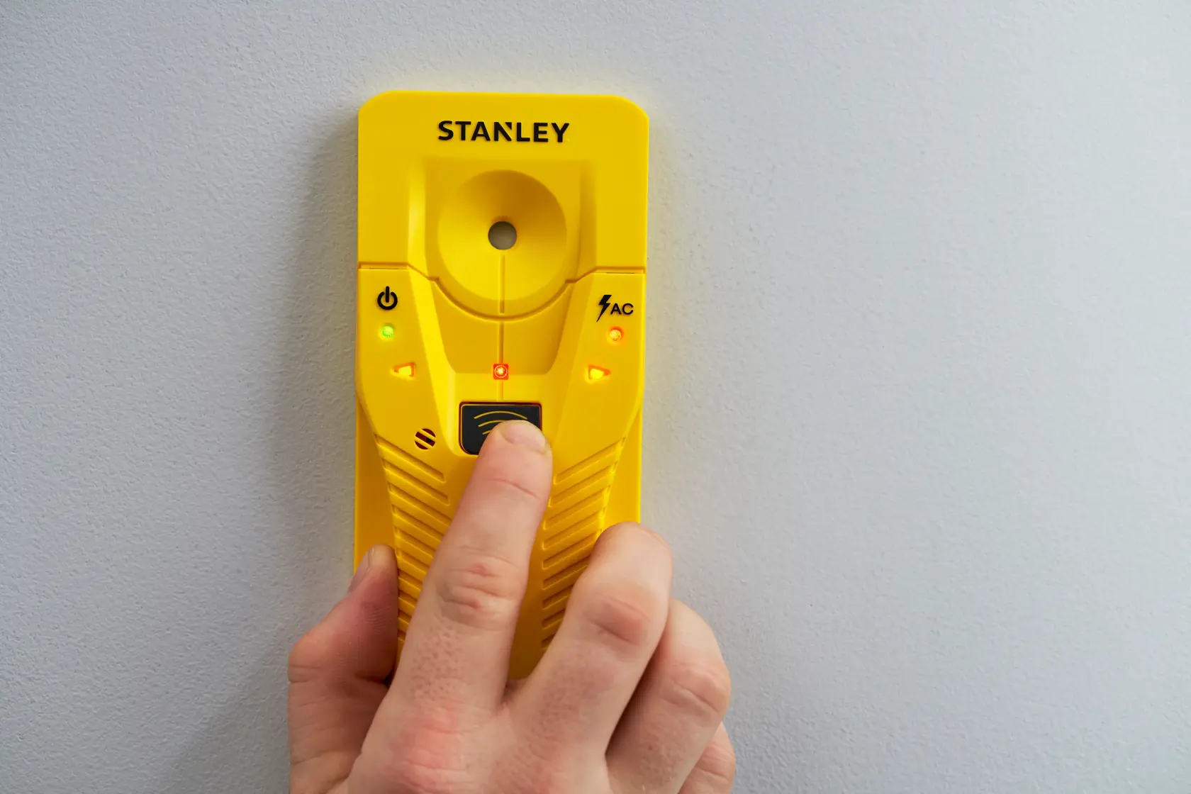 STANLEY STHT77587-0 yellow stud finder held against wall, front angle view, lights illuminated.