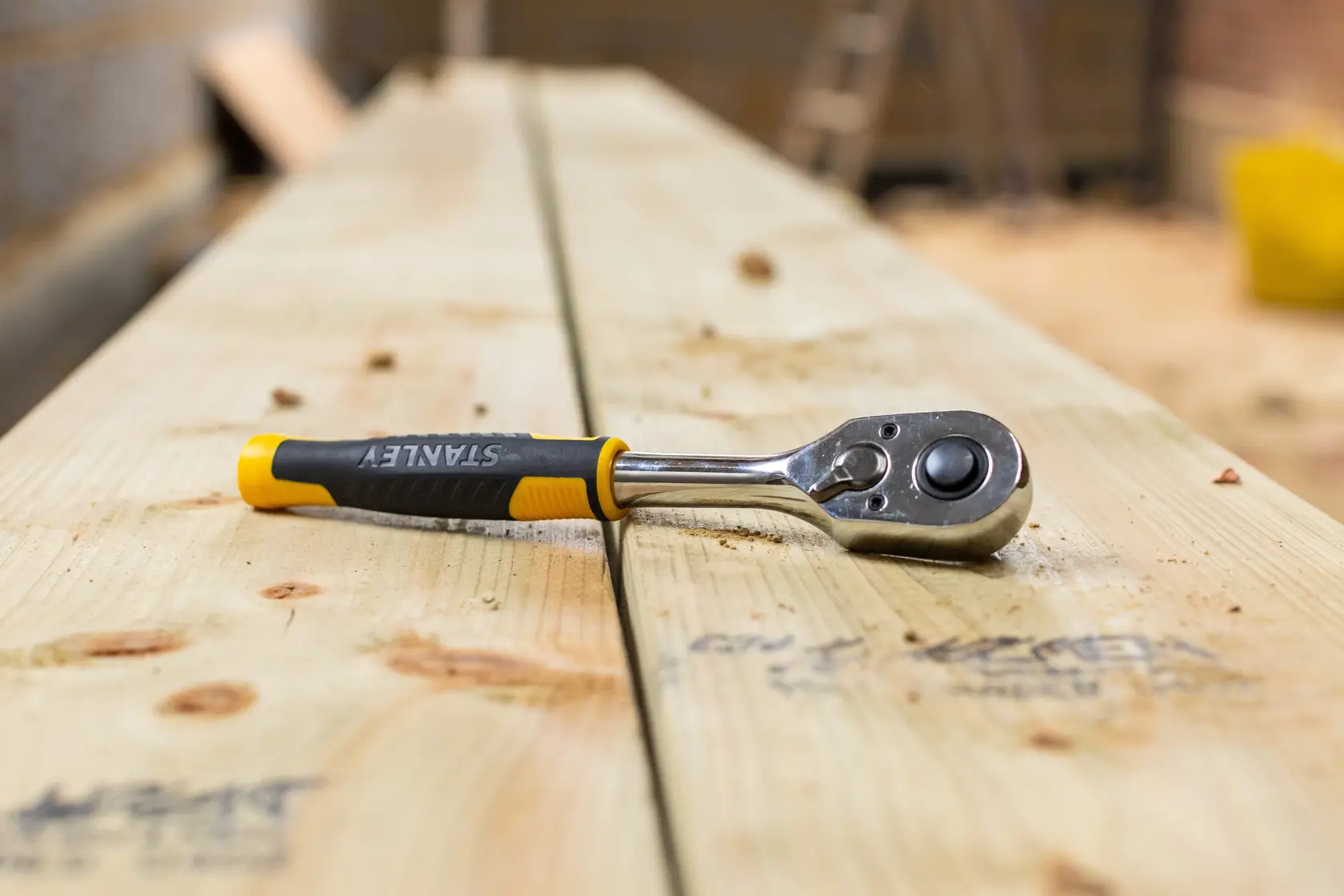 STANLEY STMT82664-0 ratchet wrench with black and yellow handle on wooden planks, side view.