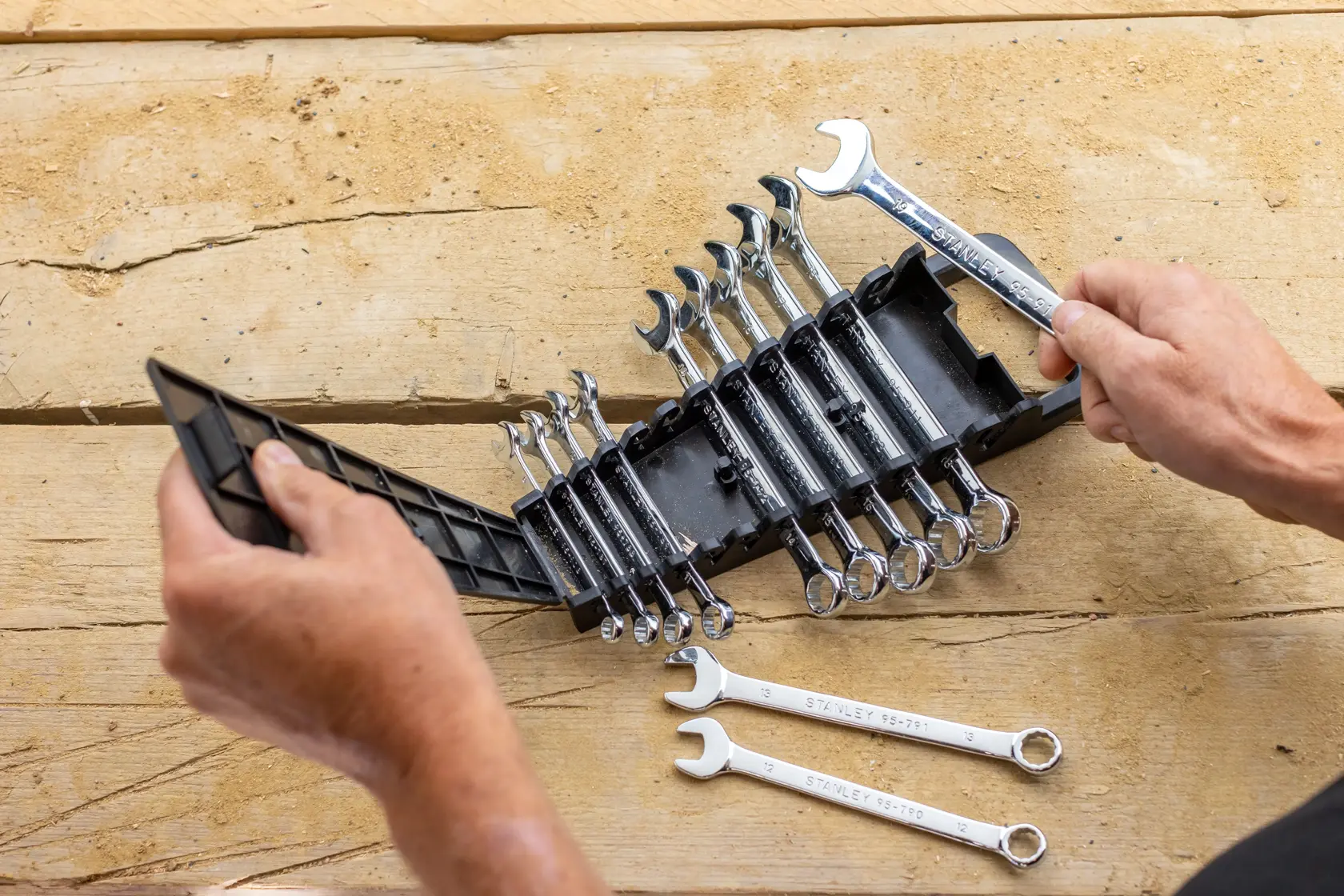 STANLEY STMT82843-0 wrench set in black plastic holder on wooden surface, two wrenches aside, hands opening case.