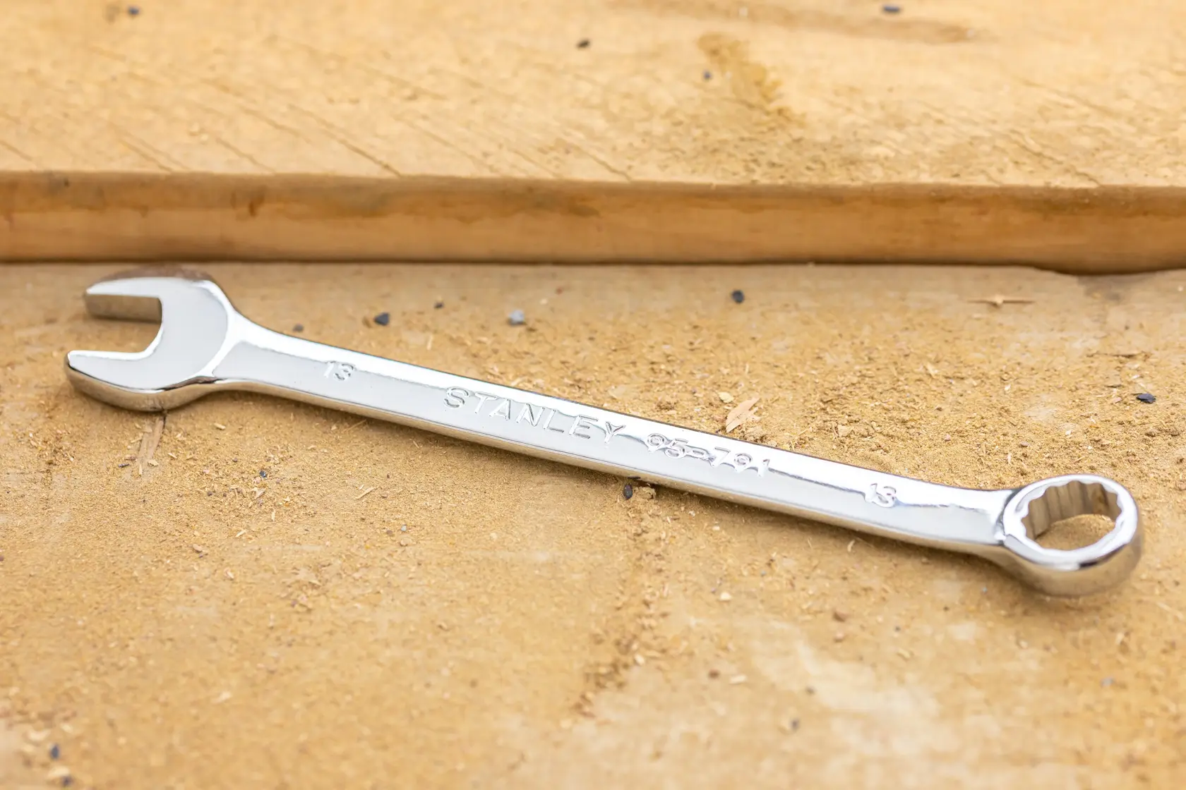 STANLEY STMT95910-0 combination wrench, silver finish, lying diagonally on a sandy wooden surface.