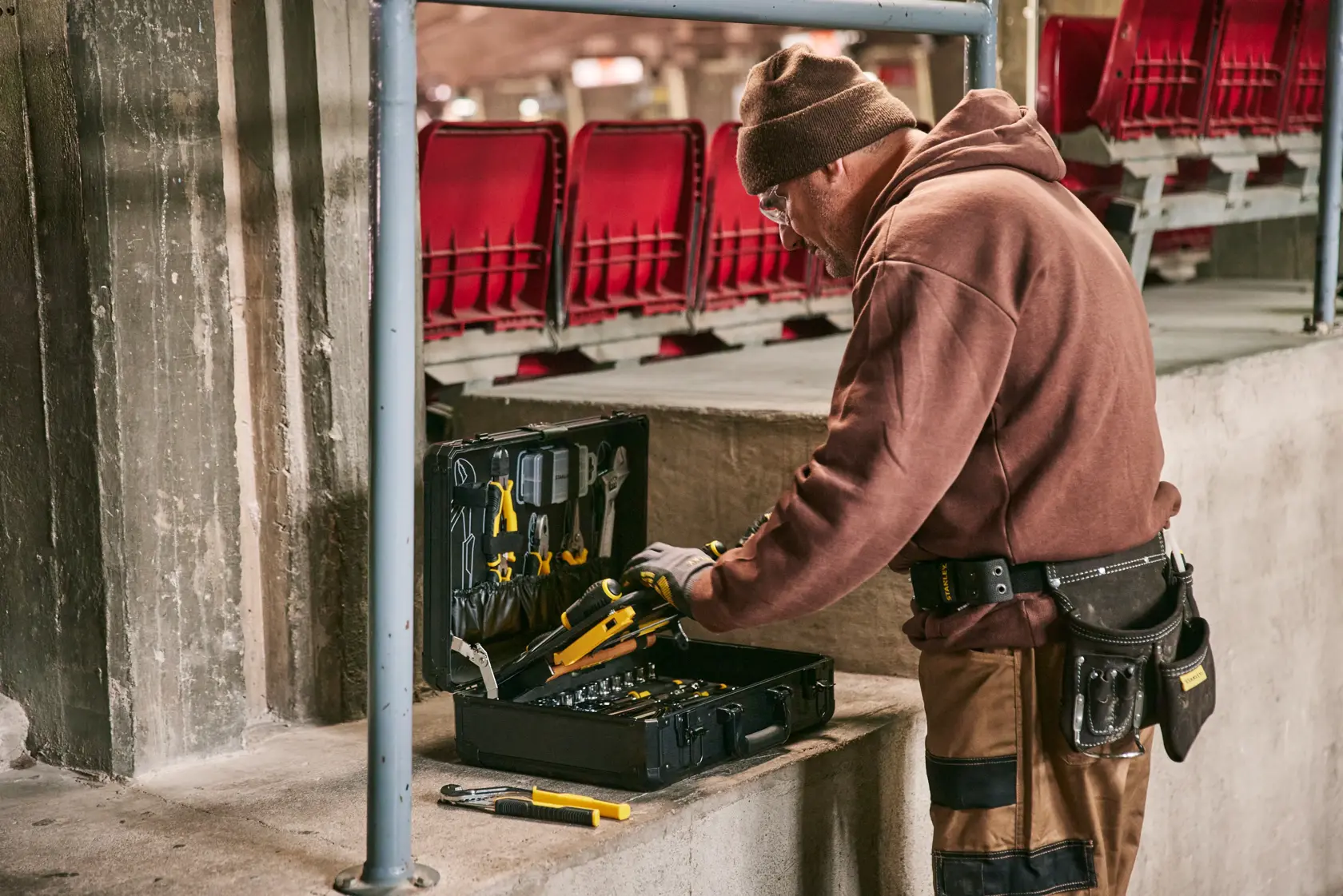 STANLEY STMT98109-1 tool case opened on concrete ledge with assorted hand tools, worker accessing tools.