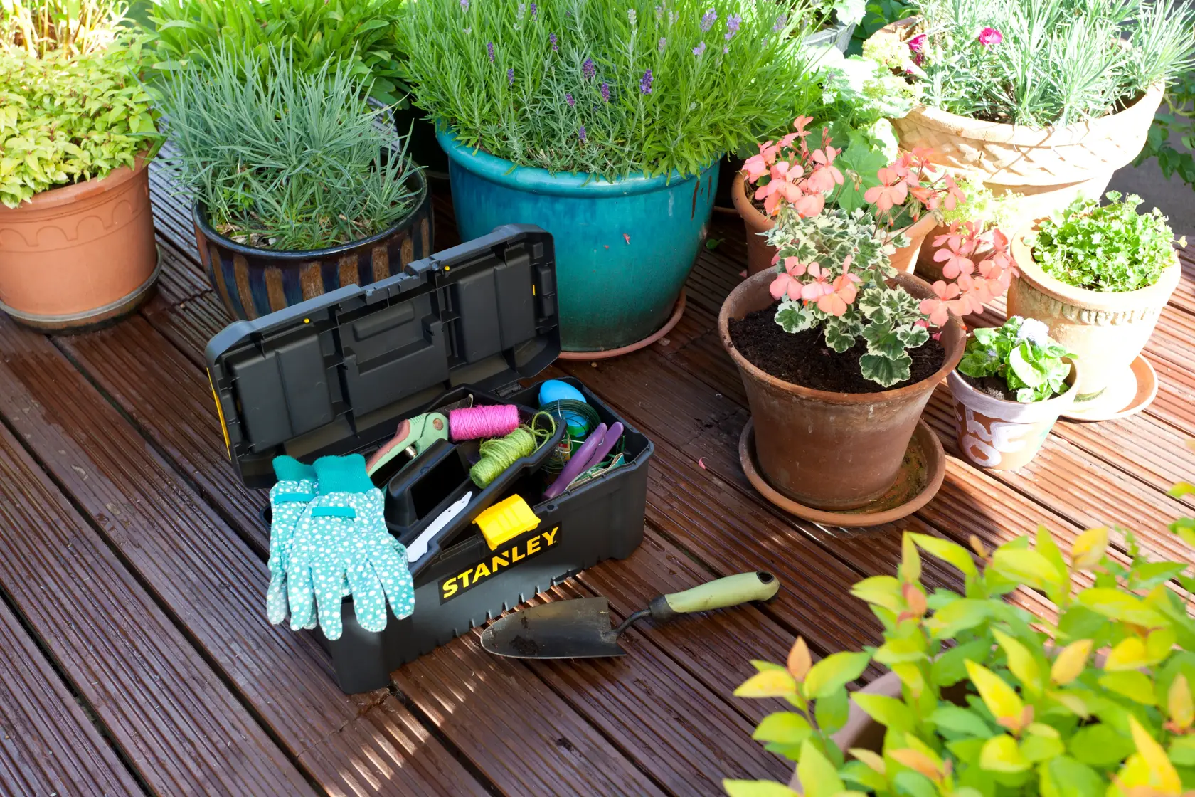 Stanley STST1-75517 toolbox with gardening tools and gloves on wooden deck near potted plants, outdoor angle.