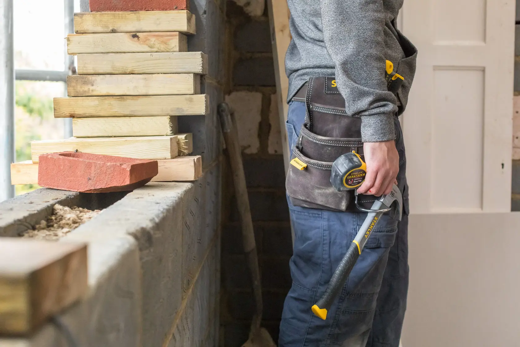 STANLEY STST1-80114 tool belt worn by worker, holding hammer and tape measure, construction site setting