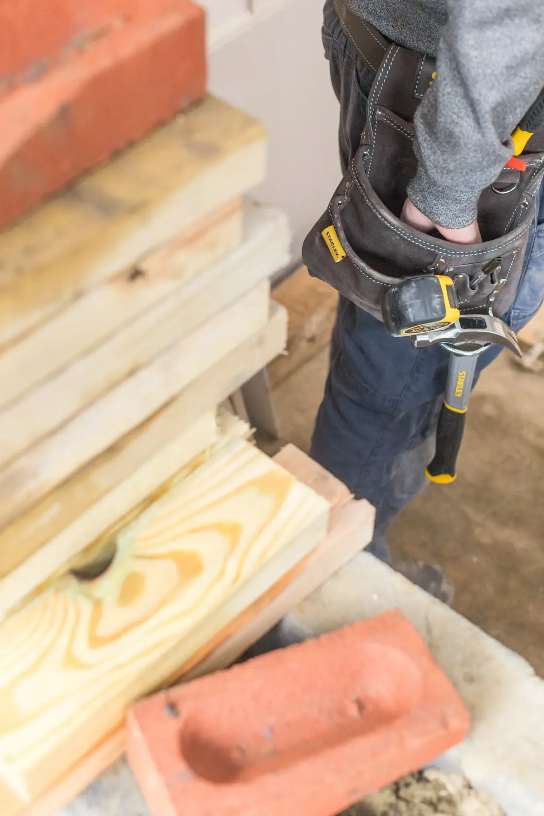 STANLEY STST1-80114 tool belt on person’s waist with hammer, close-up, construction site background.