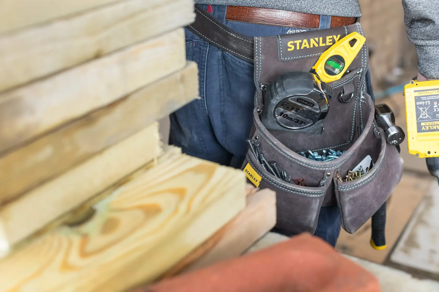 Photo of STANLEY STST1-80116 tool belt with tools and hardware, worn by a worker near stacked wooden planks.