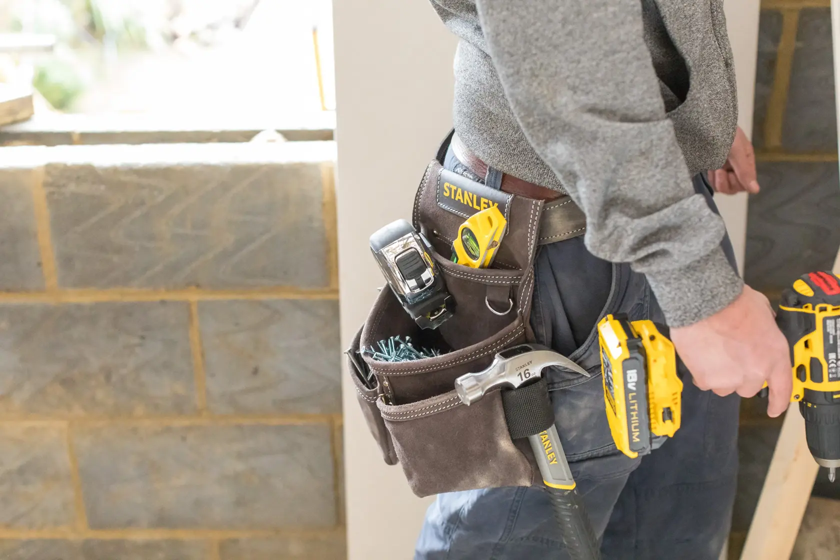 Photo of STANLEY STST1-80116 tool belt loaded with tools, worn by person in work clothes at construction site.