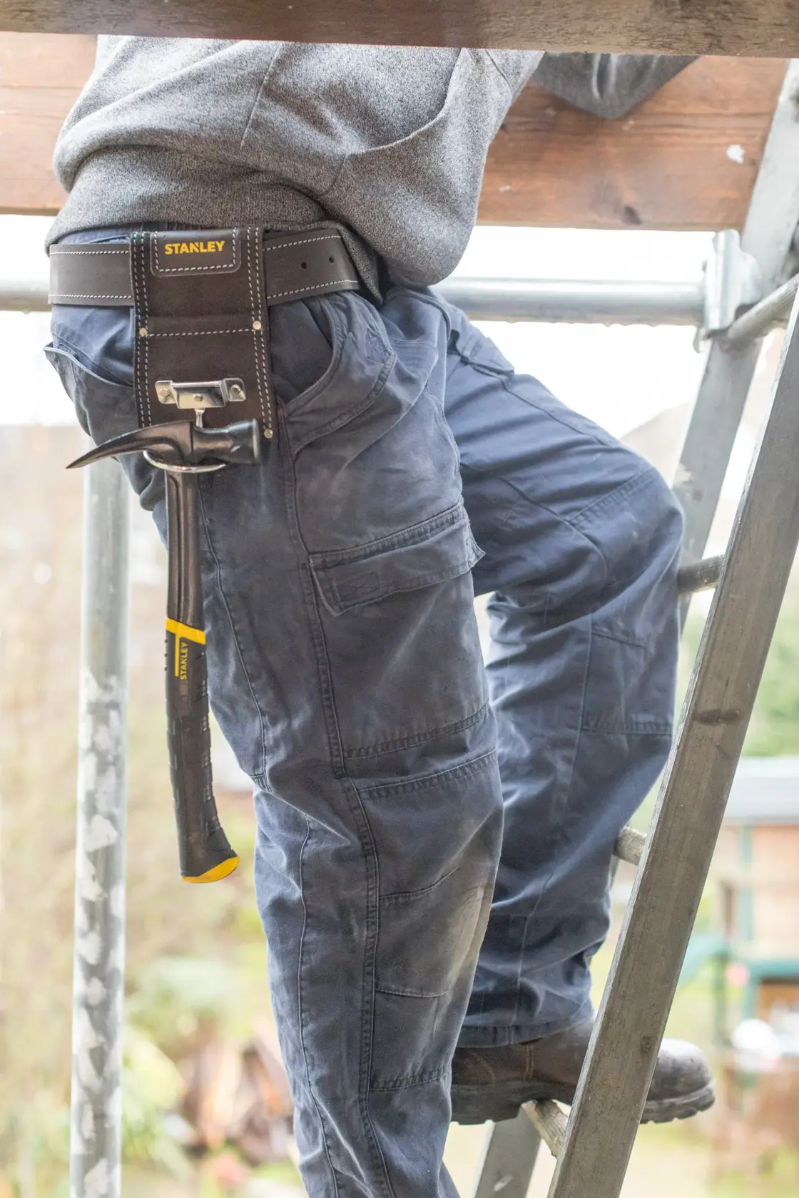 STANLEY STST1-80117 tool belt pouch holding hammer, shown on person climbing ladder, product photography.