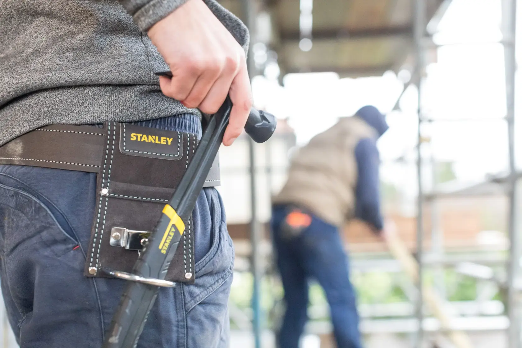 STANLEY STST1-80117 tool belt on worker’s waist with STANLEY hand tool, construction site background.