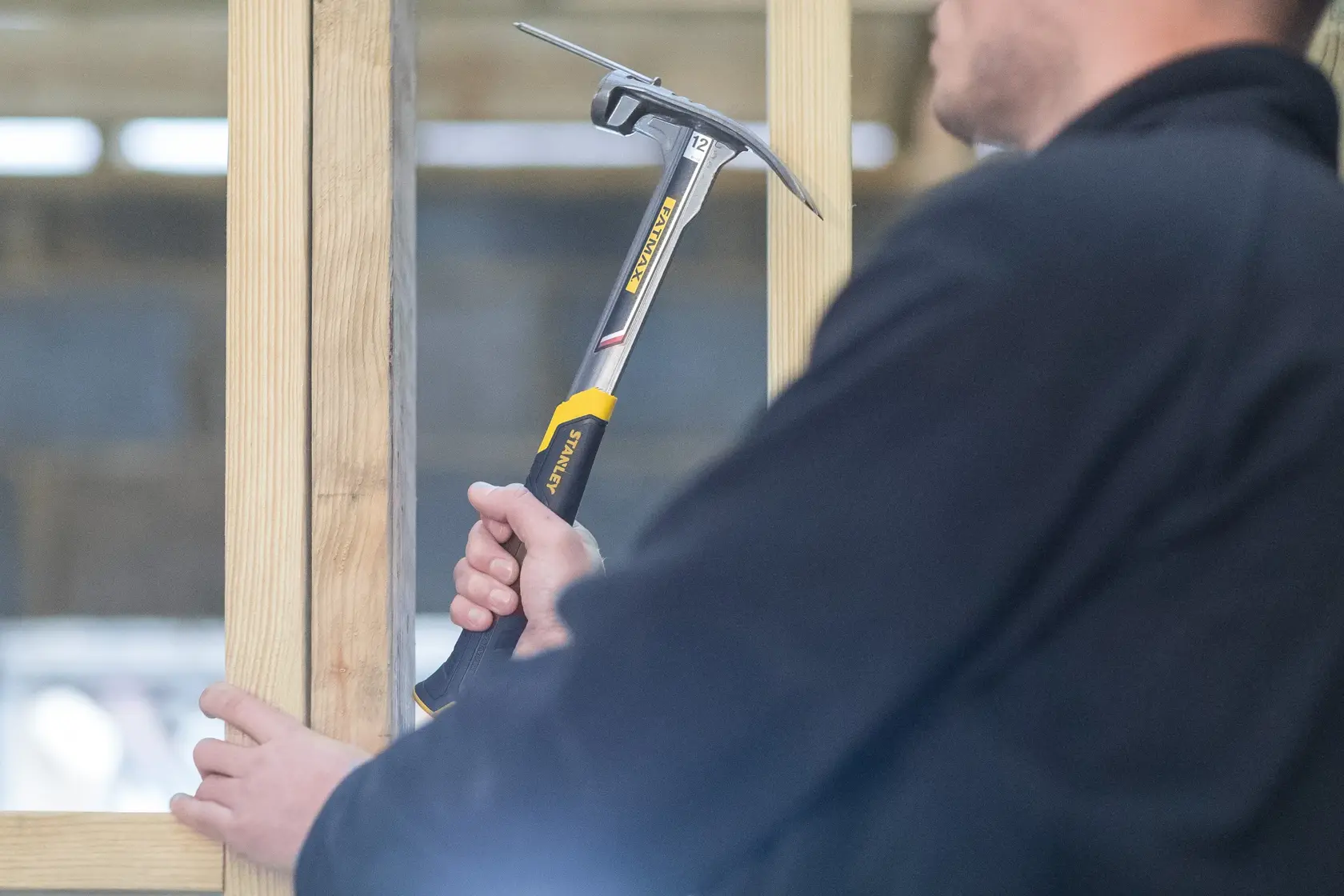 STANLEY XTHT0-51123 framing hammer in use, yellow and black handle, held against wooden beams.