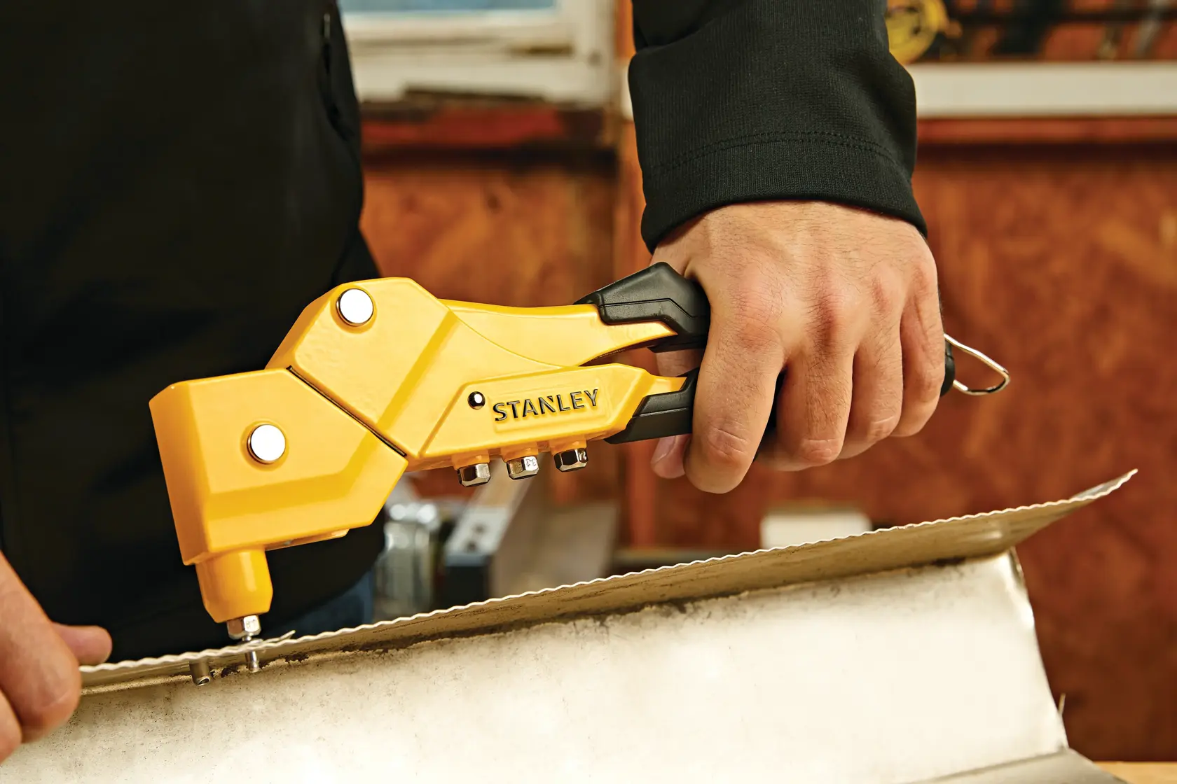 STANLEY MR77C riveter tool in yellow and black, handheld, used on a cardboard box, close-up.